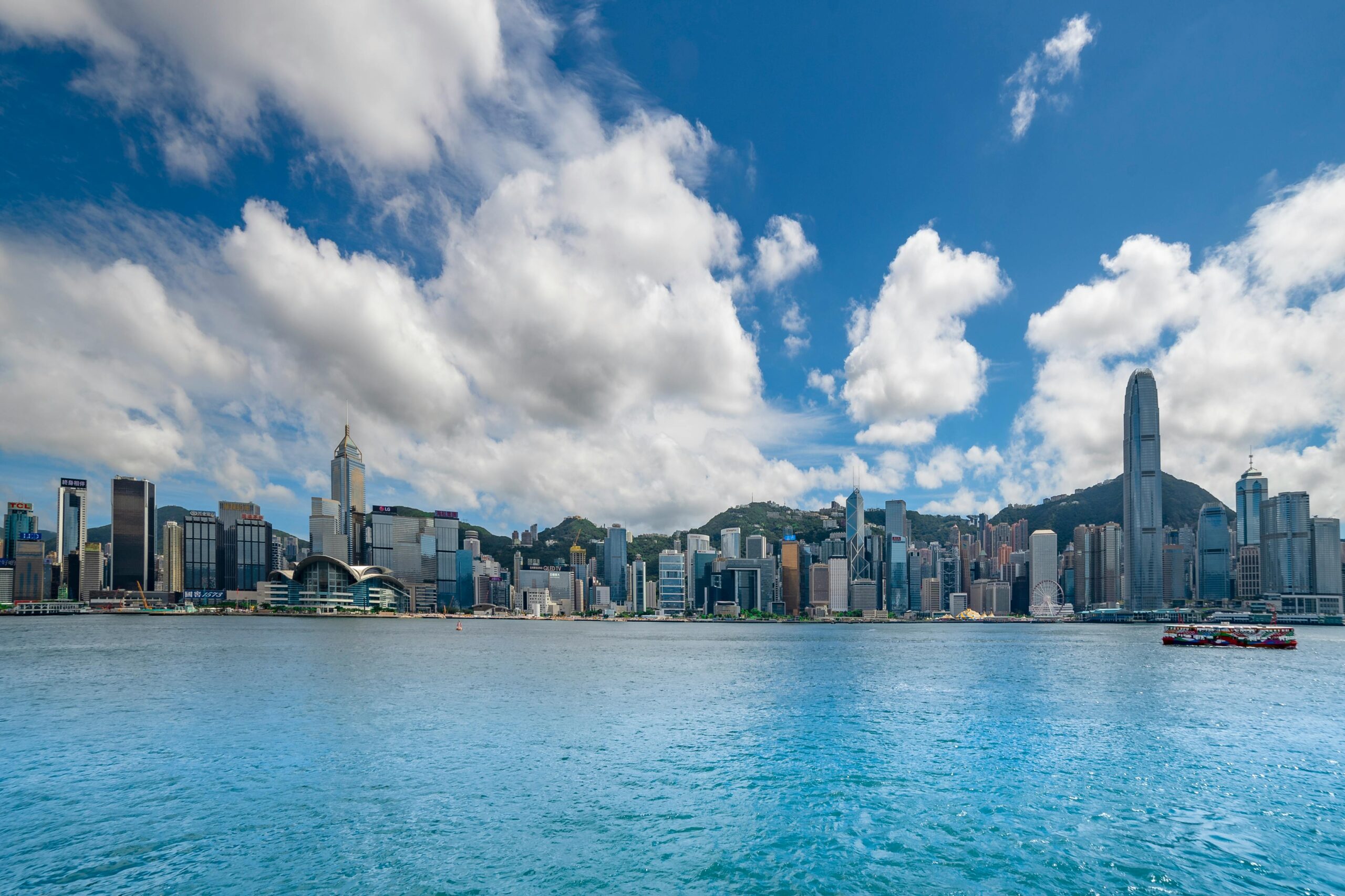 Breathtaking view of Hong Kong skyline across Victoria Harbour under a vibrant blue sky.